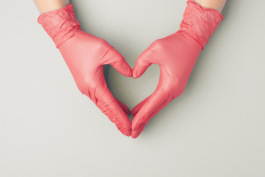 Doctor's hands in red medical gloves in shape of heart on blue background.